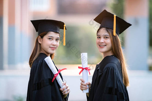 年轻快乐的亚洲女大学毕业生身着毕业礼服，身临其境，在大学校园里<strong>获得</strong>了学位证书，以庆祝她们的教育成就。教育库存照片