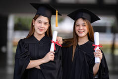 年轻快乐的亚洲女大学毕业生身着毕业礼服，身临其境，在大学校园里获得了学位证书，以庆祝她们的教育成就。教育库存照片