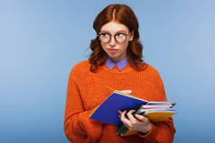 戴眼镜的红头发学生，穿着橙色毛衣，手里拿着笔记本和铅笔，用蓝色隔开