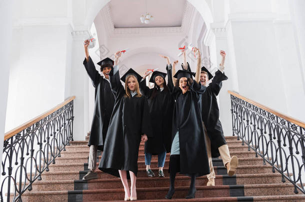 兴奋的多族裔毕业生站在大学堂的楼梯上