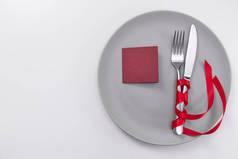 节日桌上摆满了红丝带.叉子和刀在灰色的盘子和卡片上的文字.复制空间.