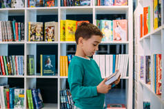 一个小男孩在书店里伸手去拿一架子儿童读物.
