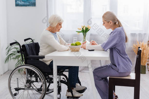 <strong>护士长</strong>为坐轮椅的残疾老年妇女注射胰岛素的侧视图