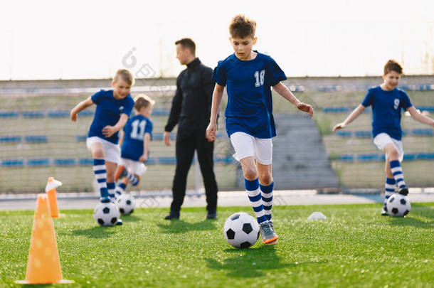 学童在足球场进行团体运动。快乐男孩踢草地上的足球球。背景下的幼儿教练