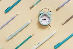 闹钟显示早上9点，该去学校上课了。用黄色和蓝色彩绘的钟表和固定学习用品进行创造性布局.