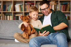 与爸爸的周末。可爱的爸爸给可爱的小男孩读书，在爱的房间里消磨时光，快乐的孩子抱着玩具玩具玩具熊，听着爸爸的仙女尾巴