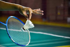 羽毛球的球拍和老的白色羽毛球手握着球员的手，在前面的球网上发球，模糊了羽毛球球场的背景和有选择的焦点.
