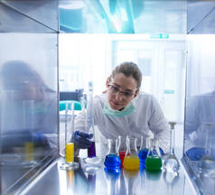 在实验室做研究实验的妇女。年轻的科学家实验室技术员，带着面罩手套，在变速箱和圆筒中监测液体.