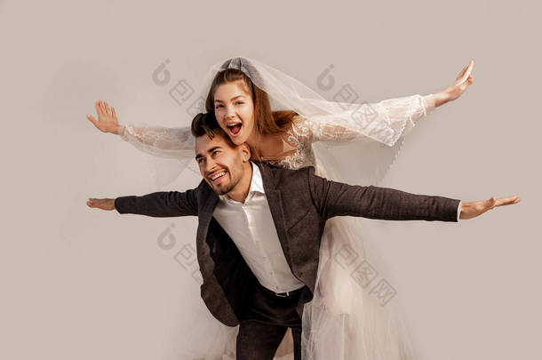 cheerful bride piggybacking on happy groom isolated on grey