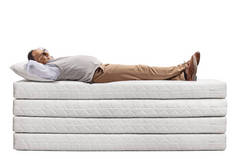 一个成熟的男人躺在一堆被白色背景隔开的床垫上