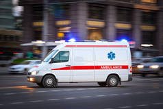 救护车在一个宽阔的城市街道上。白色的紧急车辆，装有警示灯和警笛，快速驶过一条大道。大都市救援服务运输。运动模糊和选定的焦点