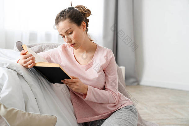 年轻的白人妇女<strong>正在看书</strong>，她坐在卧室的地板上，毛毯上