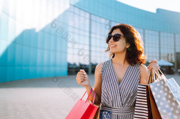 快乐的女人喜欢购物。穿着购物袋在街上走来走去的时髦女人.消费主义、销售、购买、购物、生活方式概念.