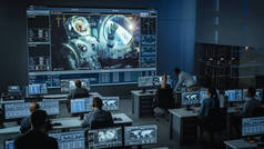 任务控制中心的一组人在空间站的大屏风上与宇航员建立了成功的视频连接。飞行控制科学家坐在计算机前.