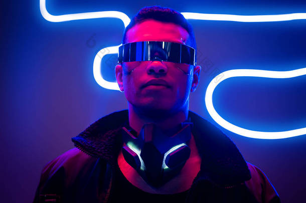 混合种族网络庞克玩家在蓝色霓虹灯附近的未来眼镜