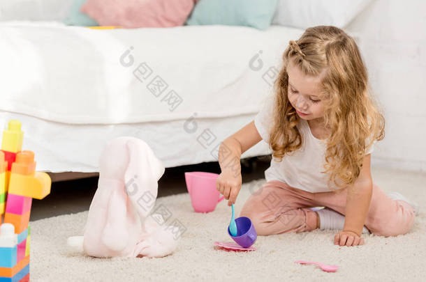 可爱的学龄前儿童玩兔子玩具和塑料杯在儿童房