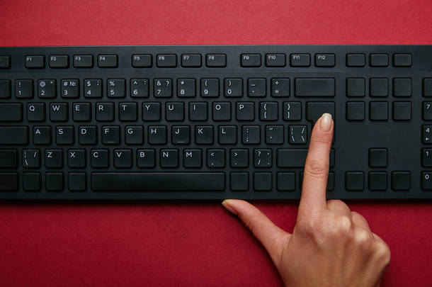 红色背景上黑色电脑键盘上的妇女按下按钮的顶部视图