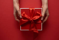 女性手拿着礼物的部份看法与丝带在红色背景