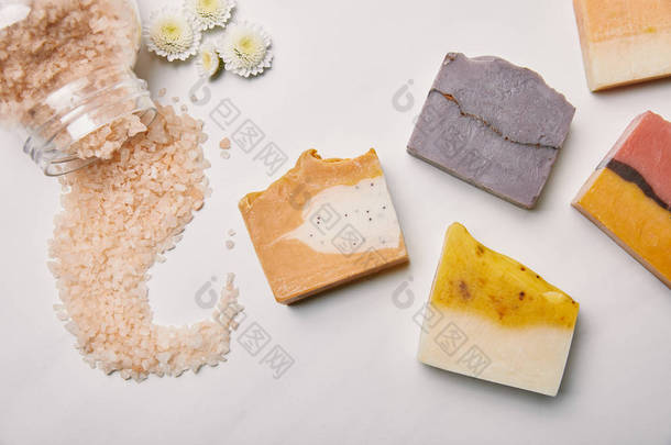 白色大理石表面的各种手工肥皂片与海盐和花朵的顶级视图