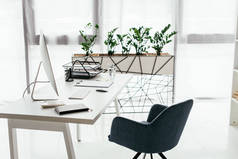 白色桌子与电脑，文件托盘，玻璃和笔记本电脑附近的办公椅和花盆与植物