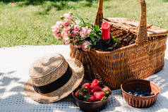 在阳光明媚的日子里，在花园中，在草帽和浆果附近的白毯子上，用玫瑰和一瓶葡萄酒装着柳条篮