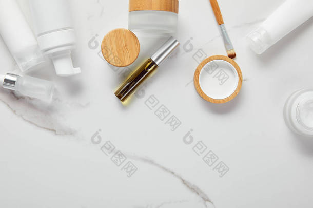 奶油管、化妆品罐、分配器和玻璃瓶的裁剪视图，在白色表面上用眼刷