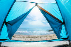 照片上是一个阳光灿烂的日子，从蓝色露营帐篷的门向海滨望去.