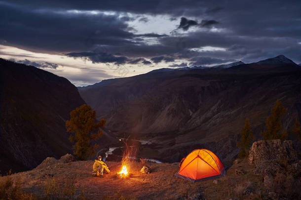 黎明时分, 一个人在灯火通明的帐篷和篝火旁