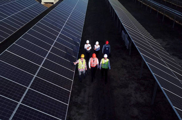 6名电气工人在长排的光伏太阳能电池板之间行走的空中<strong>变焦镜头</strong>