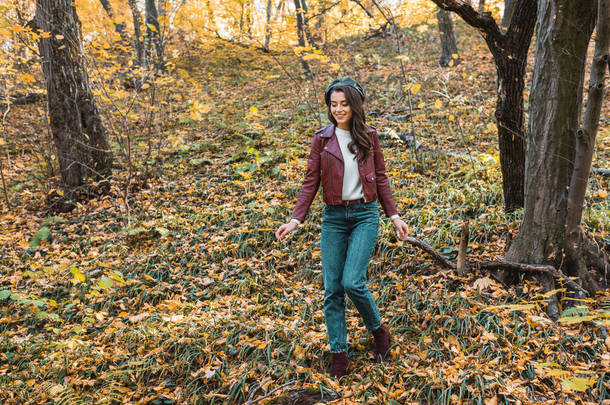 时尚年轻女子在皮革夹克和贝雷帽走在秋季公园