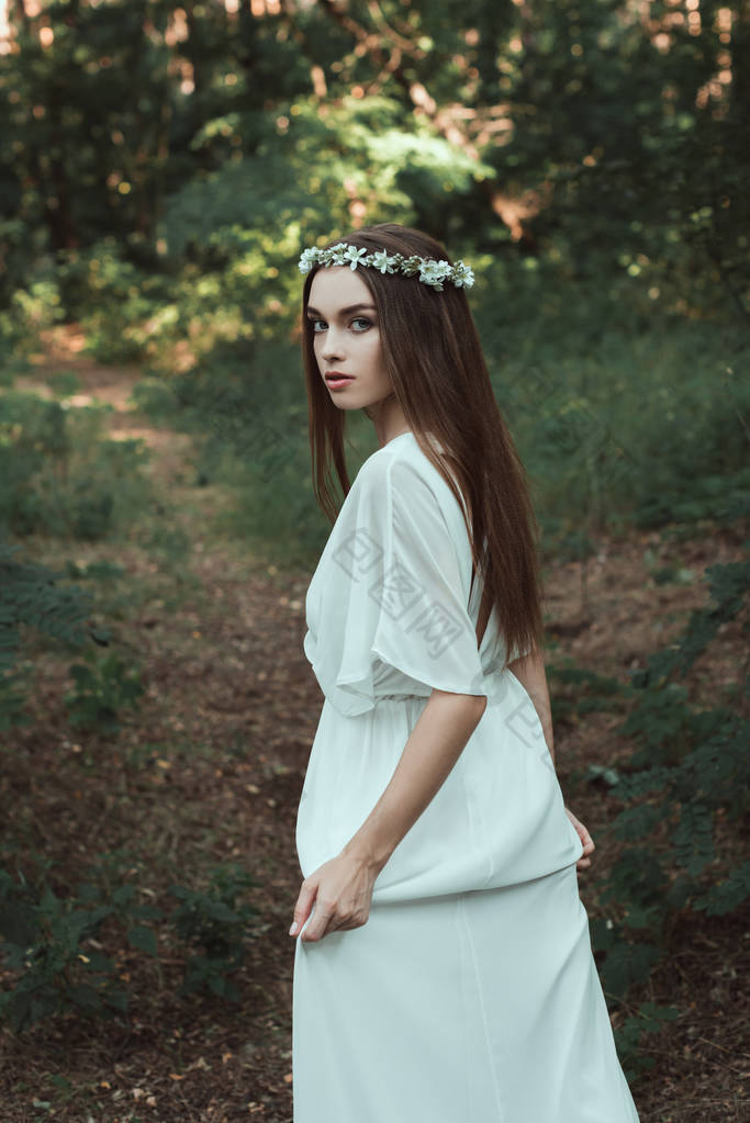 穿着白色连衣裙和花环的漂亮女孩在森林里漫