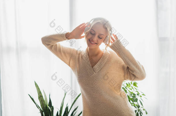 在现代公寓里，穿着无线耳机听音乐的快乐的年轻女人