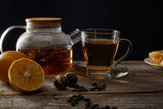 透明茶壶和茶杯与传统的盛开的茶在木桌上与柠檬隔离在黑色