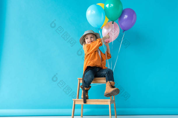 可爱的孩子在牛仔裤和橙色衬衫坐在楼梯上, 用手指指着气球
