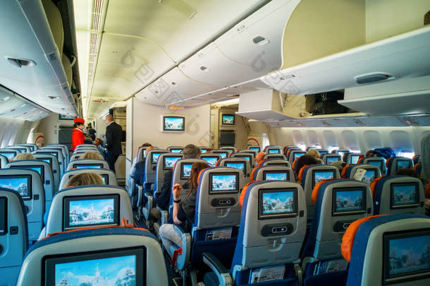 2021年6月3日，莫斯科：机舱内部，乘客座位上有监视器，戴着医疗面罩的乘客登上飞机，空姐，走道中的空姐。有选择的焦点.