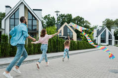 在父母附近的街道上,孩子带着五颜六色的风筝奔跑的后视图