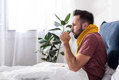 生病的年轻人坐在床上咳嗽的侧面视图