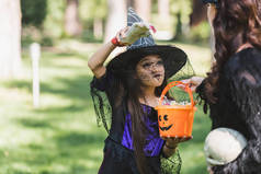 戴着女巫帽的女孩拿着装有糖果的水桶，用玩具手吓着妈妈