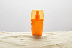 灰色背景上纹理沙上橙色瓶中的防晒霜