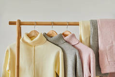 粉色、米黄色和灰色针织软毛衣和裤子挂在白色隔板架上的近景