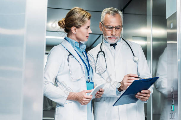 <strong>成熟男性</strong>医生显示剪贴板的女性同事与数字片在医院电梯