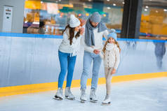 微笑的父母看着女儿, 而溜冰在溜冰场一起