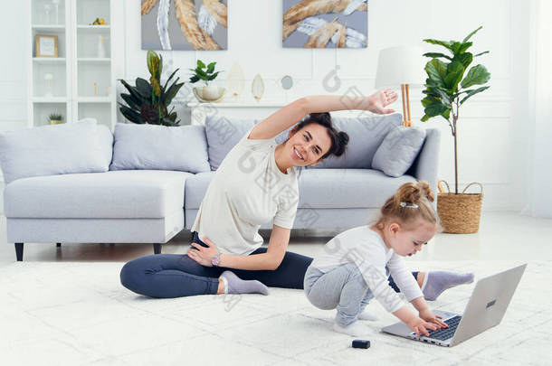 有趣的女婴<strong>在家</strong>里玩笔记本电脑，而她的运动健康的<strong>妈妈在家</strong>里接受网上瑜伽训练.
