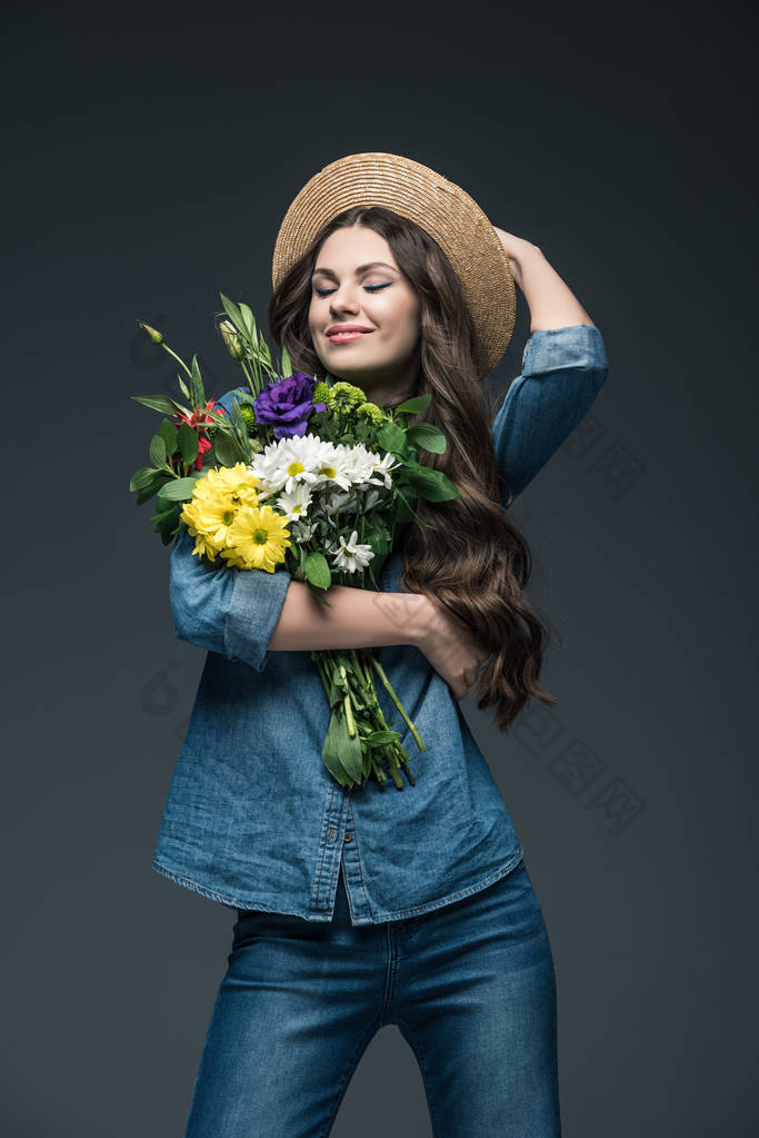 迷人的微笑女孩与闭着眼睛在牛仔服装和草帽捧着花束, 灰色隔离