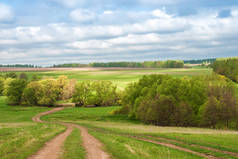 Rural dirt road in rural areas. Green fields, trees and a sky with beautiful clouds. Beautiful sprin
