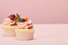 甜纸杯蛋糕与水果和浆果在粉红色的表面