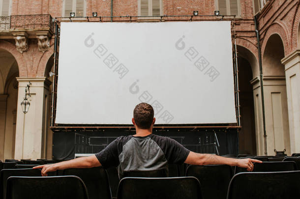 一个男人坐在大屏幕前.夏季剧场。露天电影院。空座位。这家伙喜欢视频。<strong>观看</strong>电影、<strong>电视</strong>节目、户外运动。屏幕上的空白空间