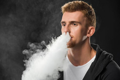 年轻的大胡子男子呼气烟雾的电子香烟包围的蒸汽云