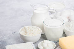 白色餐桌上的新鲜乳制品。罐子和一杯牛奶，一碗酸奶油，干酪和烤面粉和莫扎雷拉。鸡蛋和奶酪。文本空间