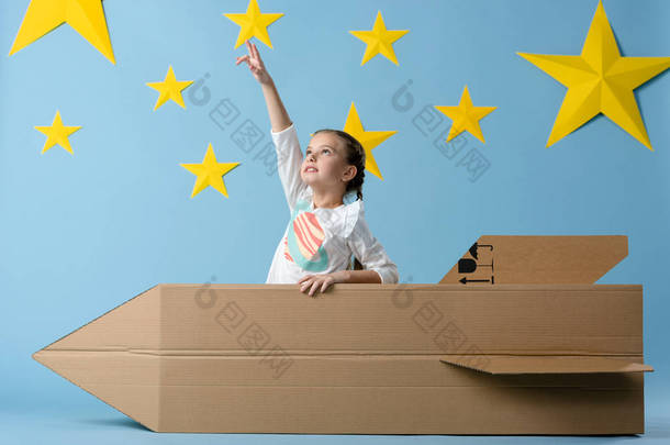 孩子与纸板火箭用手指指向星星在蓝色<strong>星空背</strong>景